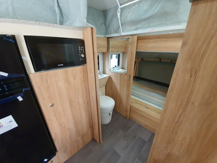 Compact RV rental interior: microwave, toilet, and sleeping area visible. Features a space-saving design for travel.. Golf Maxxi 501-1 2021