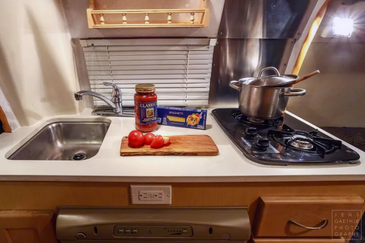 Compact RV rental kitchen setup with stove, sink, and ingredients for cooking spaghetti.. Ford FordE350 2006