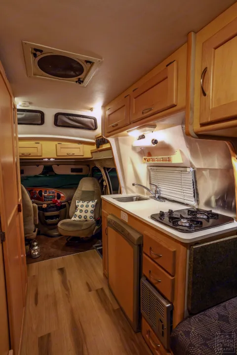 RV rental interior: full kitchen with stove & sink, swivel seats, and ample storage. Ideal camper van for adventures.. Ford FordE350 2006