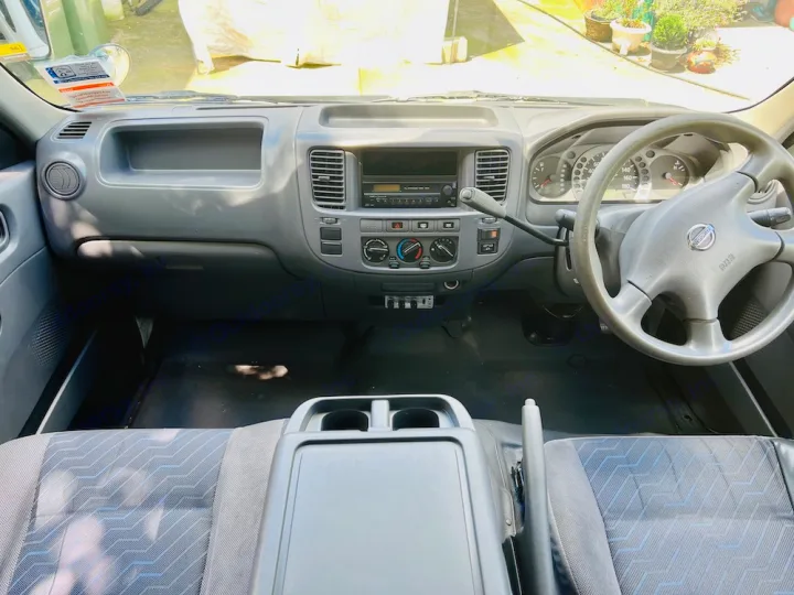 Detailed view of an RV rental's functional Nissan vehicle interior, including dashboard, steering wheel, and front seats.. Nissan Caravan 2005