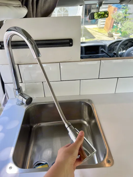 RV rental kitchen: A hand demonstrates the extended pull-down faucet over the stainless steel sink.. Nissan Caravan 2005