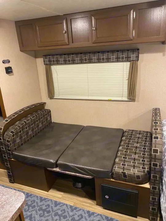 RV rental interior featuring a dinette with brown cushions, convertible seating, overhead cabinets, and window blinds.. Shasta Oasis 18BH 2018