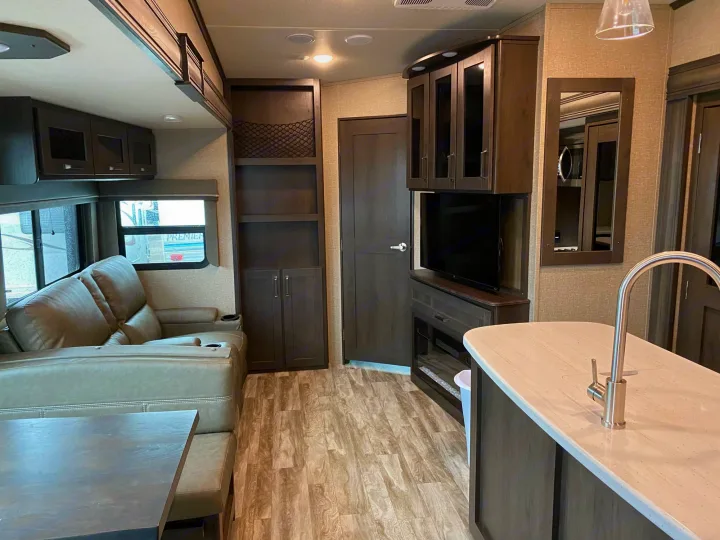 Spacious RV rental interior: living area with sofa & dining, modern kitchen island, TV, and dark wood storage.. Grand Design Reflection 2022