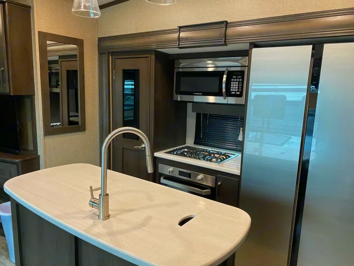 Modern RV rental kitchen featuring an island with sink, microwave, stove, oven, and large refrigerator. Spacious and well-equipped interior.. Grand Design Reflection 2022
