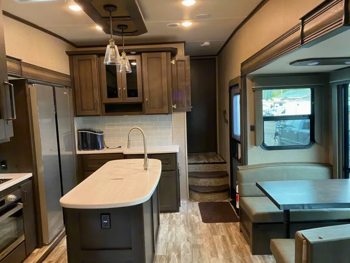 Inside a modern RV rental: sleek kitchen island, dark cabinetry, and comfy dinette, ready for your next road trip.. Grand Design Reflection 2022