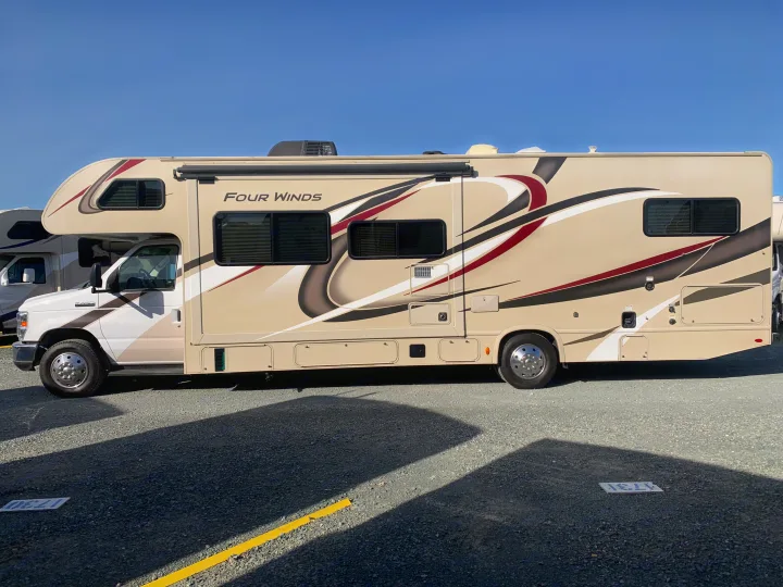 A beige Four Winds motorhome, an ideal rv rental, is parked outdoors under a clear blue sky, seen from the side.. Thor Motor Coach Four Winds 2020