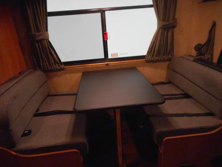 RV rental dinette area: Two cozy benches with a dark table between them, and a window with brown curtains.. Thor Majestic 2017