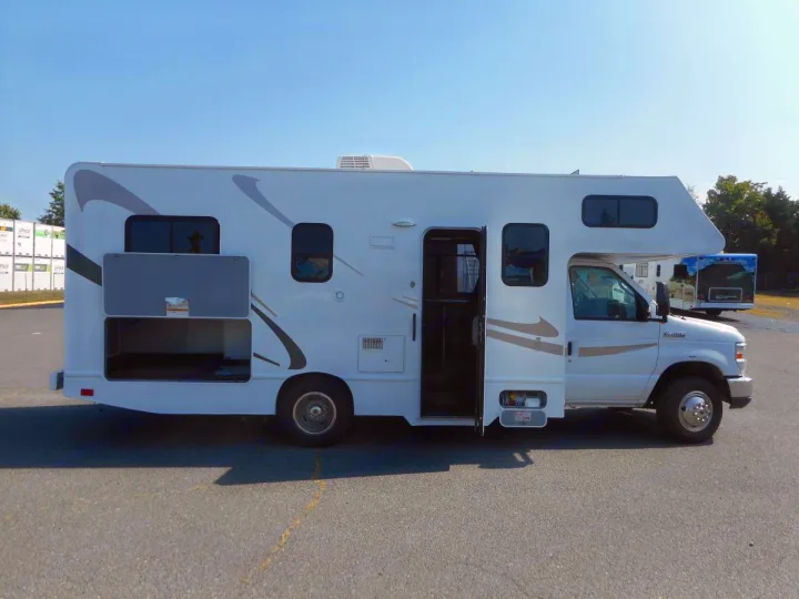 Side view of a white Class C RV rental with its main entry door and a large storage compartment open.. Thor Majestic 2017