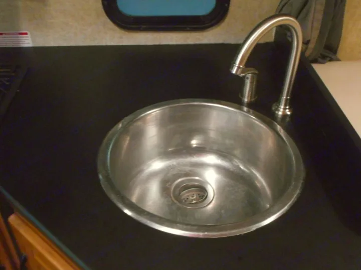 Compact RV rental kitchen sink and faucet on dark countertop. A clean, stainless steel basin for your travels.. Thor Majestic 2017