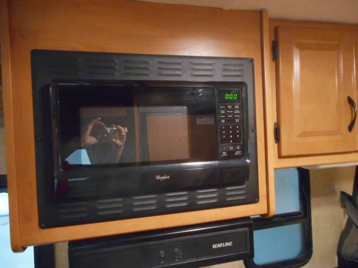 RV rental kitchen featuring a Whirlpool microwave showing 0:00, integrated into wooden cabinets above a VENTLINE unit.. Thor Majestic 2017