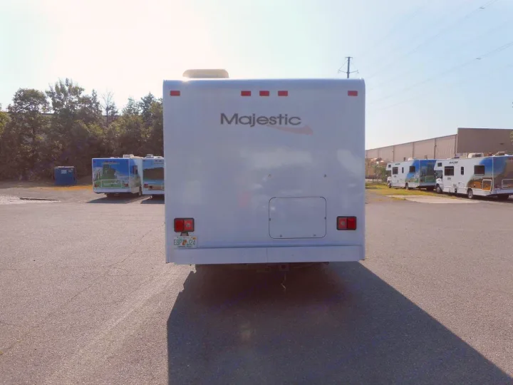 Rear view of a white Majestic RV, likely an RV rental, parked in a sunny lot with other recreational vehicles.. Thor Majestic 2017