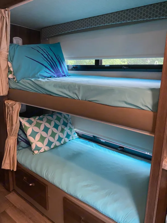 RV rental with cozy bunk beds. Features light blue bedding, patterned pillows, window shades, and storage for comfortable travel.. Jayco Greyhawk 2019