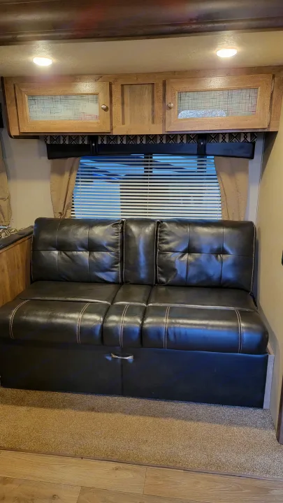 RV rental: Cozy interior featuring a dark L-shaped sofa with white stitching, wood cabinets, and vertical window blinds.. Forest River Puma 2017