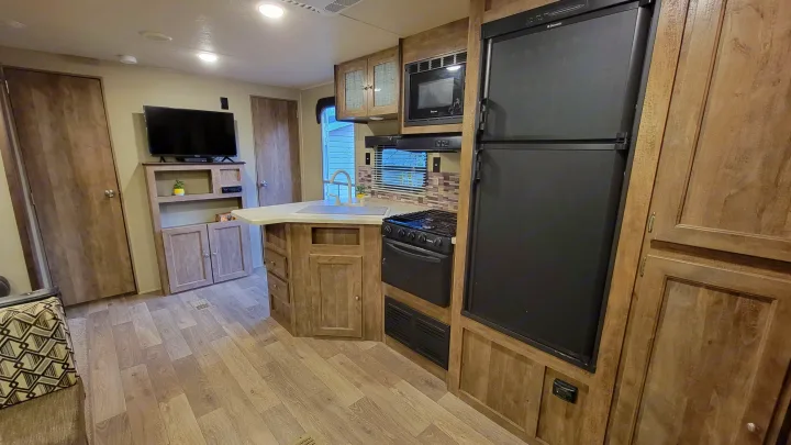 Compact & functional RV rental interior: kitchen with microwave, fridge, stove; living area with TV, wood floors.. Forest River Puma 2017