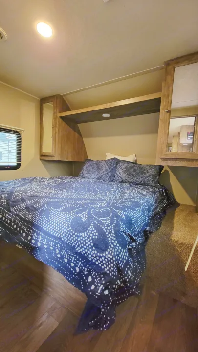 RV rental bedroom: a compact space with blue patterned bedding, an overhead mirror, and built-in storage.. Forest River Puma 2017