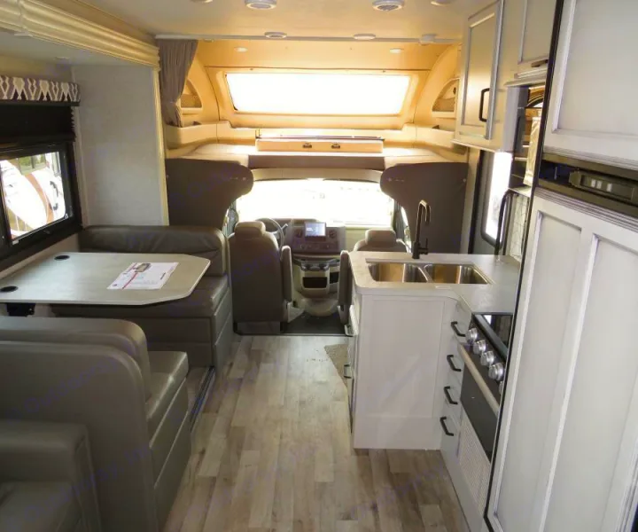 View inside an RV rental showing its compact kitchen, dinette, and front driver's area with an overhead bunk.. Entegra Coach Odyssey 30Z 2022