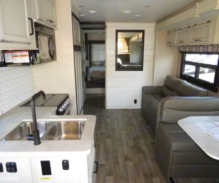 Spacious RV rental interior with a modern kitchen, living area, and a bedroom visible further back.. Entegra Coach Odyssey 30Z 2022