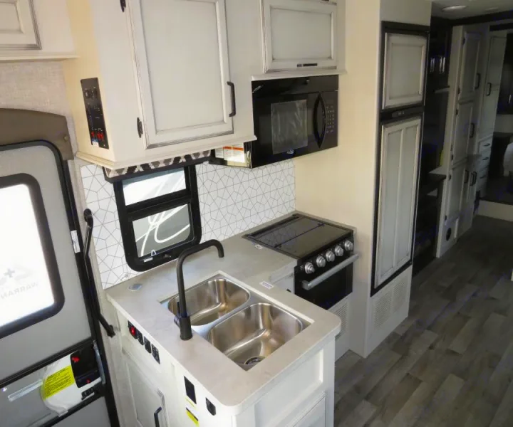 Modern RV rental kitchen with double sink, stove, microwave, fridge, and geometric backsplash.. Entegra Coach Odyssey 30Z 2022