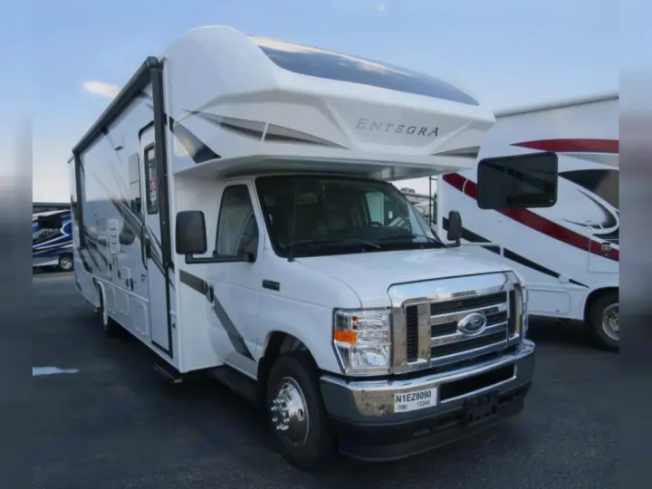 White Entegra Class C RV rental on a Ford chassis, with grey and black graphics, parked in a lot under a clear sky.. Entegra Coach Odyssey 30Z 2022