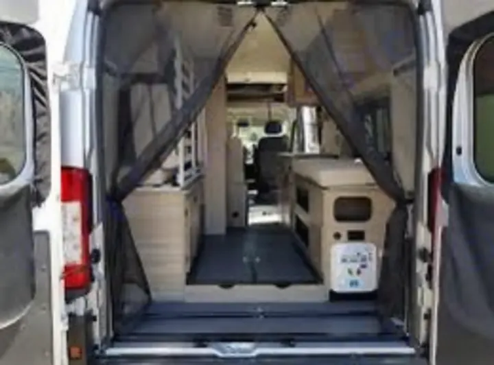 This RV rental campervan's rear view through an open bug screen, revealing a functional interior with a compact kitchen.. Winnebago Solis 59PX 2022