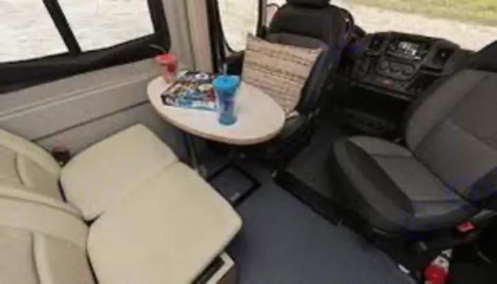 RV rental interior: Swivel front seats, small table with drinks, and a bench offer comfy travel space.. Winnebago Solis 59PX 2022