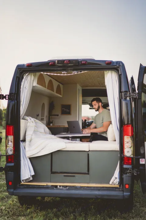 Man on laptop inside a black, converted RV rental van with rear doors open. Perfect for remote work and digital nomad adventures.. Other Other 2015