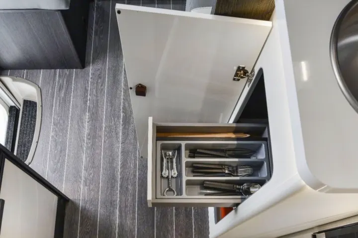 Inside an RV rental kitchen: open drawer with cutlery organizer and corkscrew, above dark wood-look floor.. Roller Team 685 Zefiro 2022