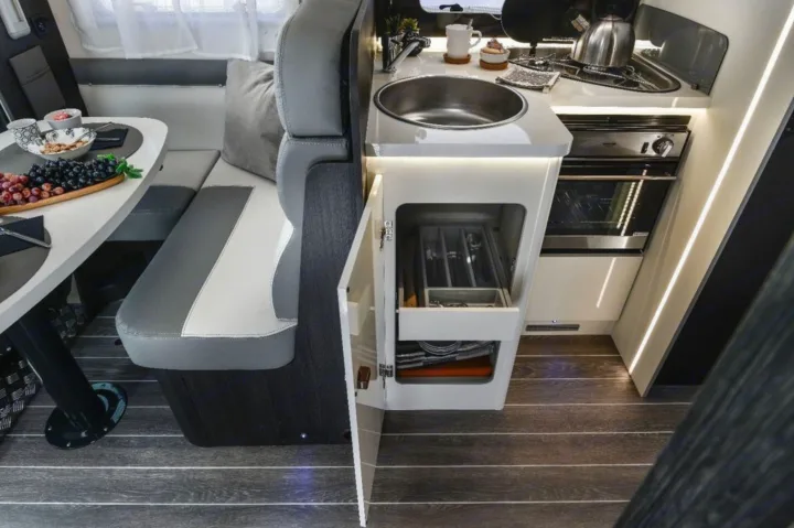 Compact rv rental interior showing a dining area with fruit, kitchenette with sink & oven, & open cabinet with cutlery.. Roller Team 685 Zefiro 2022