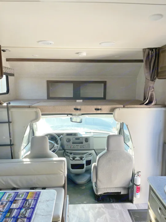 Inside this **RV rental**, see the front cab, spacious overhead bunk, and part of the living area. A comfortable **motorhome** interior.. Gulf Stream Conquest 2021