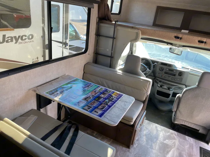 Spacious Class C **rv rental** interior: dinette, overhead bunk, and cockpit area. Jayco brochure on table.. Gulf Stream Conquest 2021