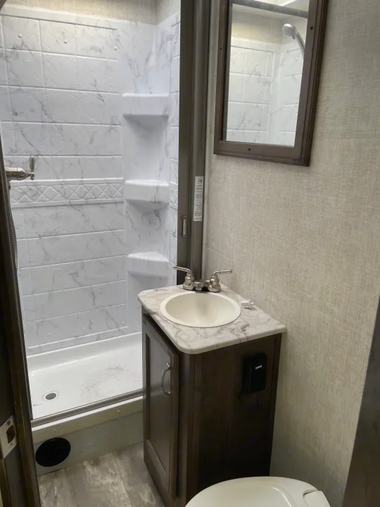 RV rental bathroom with a compact shower, vanity, sink, and toilet, offering essential amenities for travel.. Gulf Stream Conquest 2021