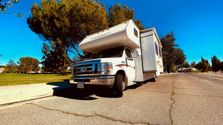 White Winnebago RV rental parked on a sunny residential street with green trees and a clear sky.. Winnebago 31k 2015