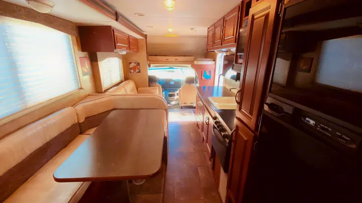 Step inside this inviting RV rental! Features a comfortable dinette, full kitchen, and views of the driver's cockpit.. Winnebago 31k 2015