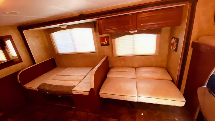 Cozy RV rental interior featuring two convertible dinette beds, windows, and overhead cabinets.. Winnebago 31k 2015