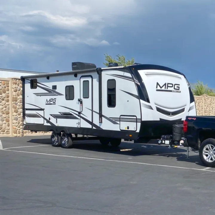 This white and black travel trailer, likely an RV rental, is hitched to a black truck, ready for a road trip or camping adventure.. Cruiser RV MPG Ultra Lite 2500BH 2021