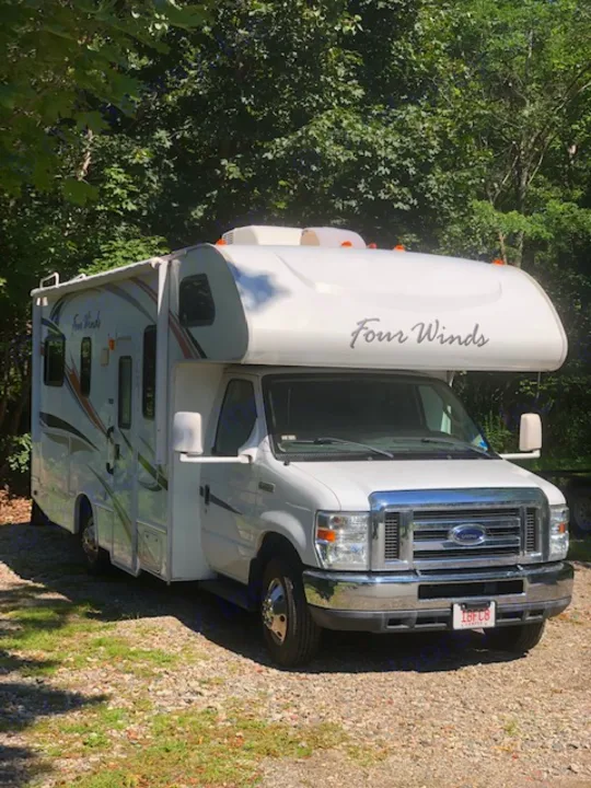 White Four Winds Ford Class C rv rental, a motorhome, parked on gravel with green trees in the background.. Four Winds Four Winds Motorhome 2011