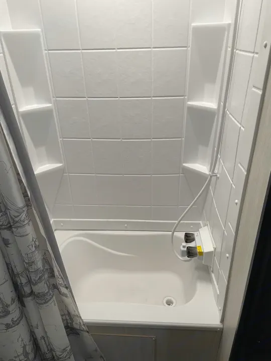 Compact, white shower stall in an RV rental, featuring built-in shelves, shower head, and a patterned curtain.. Forest River Cherokee Wolf Pup 2019
