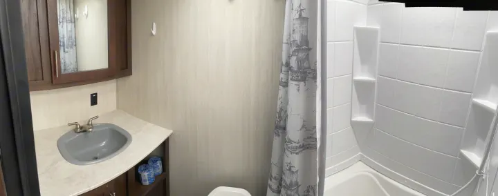Inside an RV rental bathroom: vanity, mirror, toilet, and shower with a nautical-themed curtain and shelving.. Forest River Cherokee Wolf Pup 2019