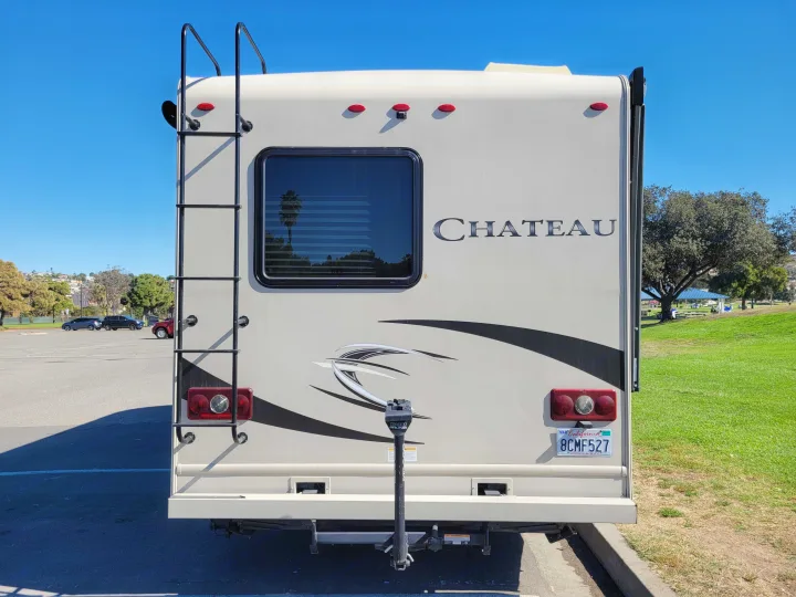Rear of a Chateau RV rental. Features include a ladder, window reflecting a palm tree, and a bike rack attachment.. Thor Chateau 2018