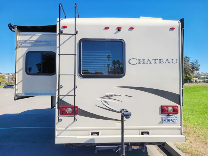 Rear of a Chateau RV rental, parked outdoors. Features include an open slide-out, ladder, camera, and bike rack.. Thor Chateau 2018