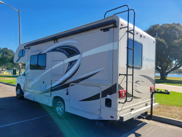 Beige Thor Chateau Class C RV rental parked, showing rear ladder, bike rack, and side graphic design for road trips.. Thor Chateau 2018
