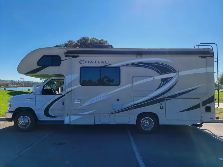 A beige Chateau rv rental parked by a scenic lake, ready for outdoor adventures and travel.. Thor Chateau 2018