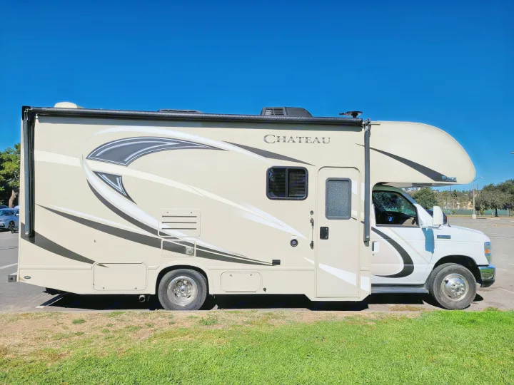 Side view of a beige Thor Chateau Class C RV rental, with graphic designs, parked on a sunny day under blue sky.. Thor Chateau 2018
