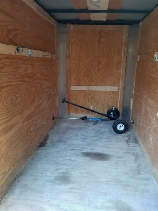 Interior of an empty wooden cargo trailer, suitable for RV rental, featuring wall hooks and a wheeled dolly on the grey floor.. Other Other 2012