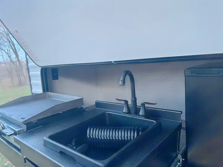 RV rental's outdoor kitchen, featuring a griddle/grill and a sink with a dish rack, perfect for camping.. Palomino Puma 2022