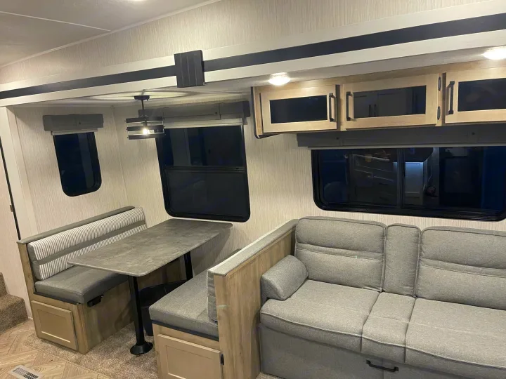 Modern RV rental living space with a gray dinette, table, sofa, windows, and light wood overhead cabinets.. Palomino Puma 2022