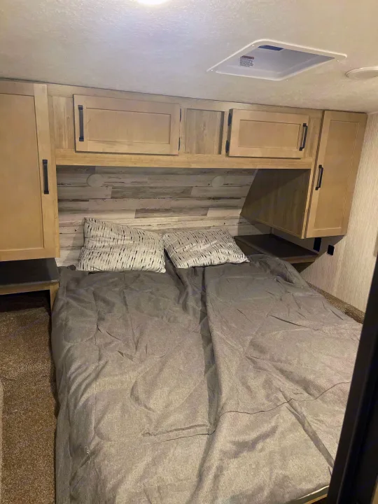 Cozy RV rental bedroom with a comfortable bed, light wood overhead cabinets, and shelves. Ideal for a relaxing journey.. Palomino Puma 2022