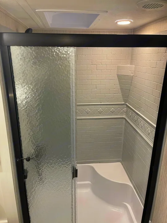 RV rental shower: textured glass door, white subway tile walls with decorative trim, built-in corner shelf, and bright ceiling lights.. Palomino Puma 2022