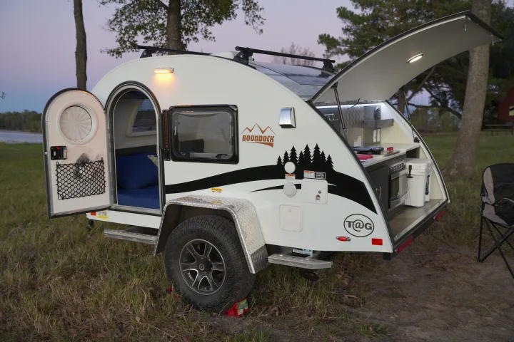 Compact T@G Boondock RV rental with open side door and rear kitchen hatch, ready for camping in the outdoors at dusk.. nuCamp T@G 2021
