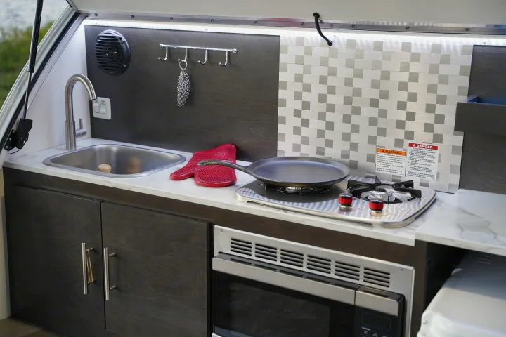 Convenient outdoor kitchen in an RV rental with sink, stove, microwave, and cabinets, ready for your camping trips.. nuCamp T@G 2021
